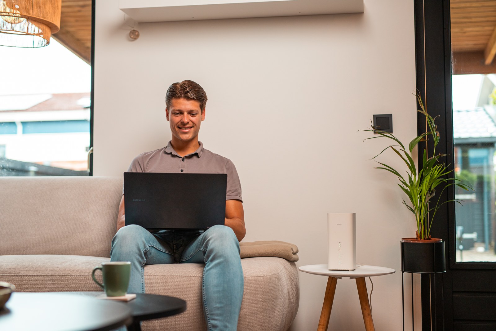 Man zit met een laptop op de bank, met het 5G-modem op de bijzettafel naast hem