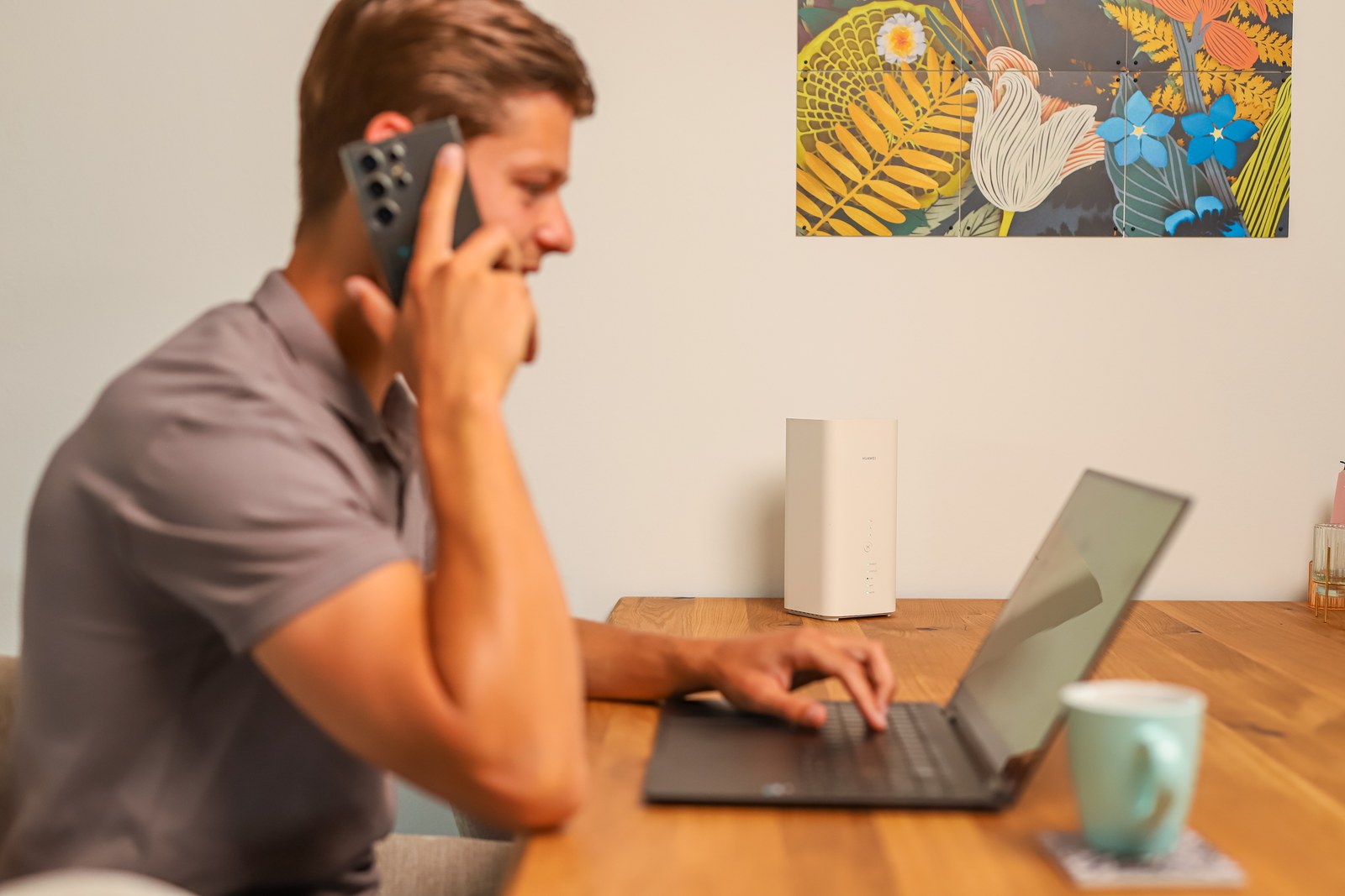 Man aan tafel met de telefoon aan het oor en een laptop, het 5G-modem naast hem