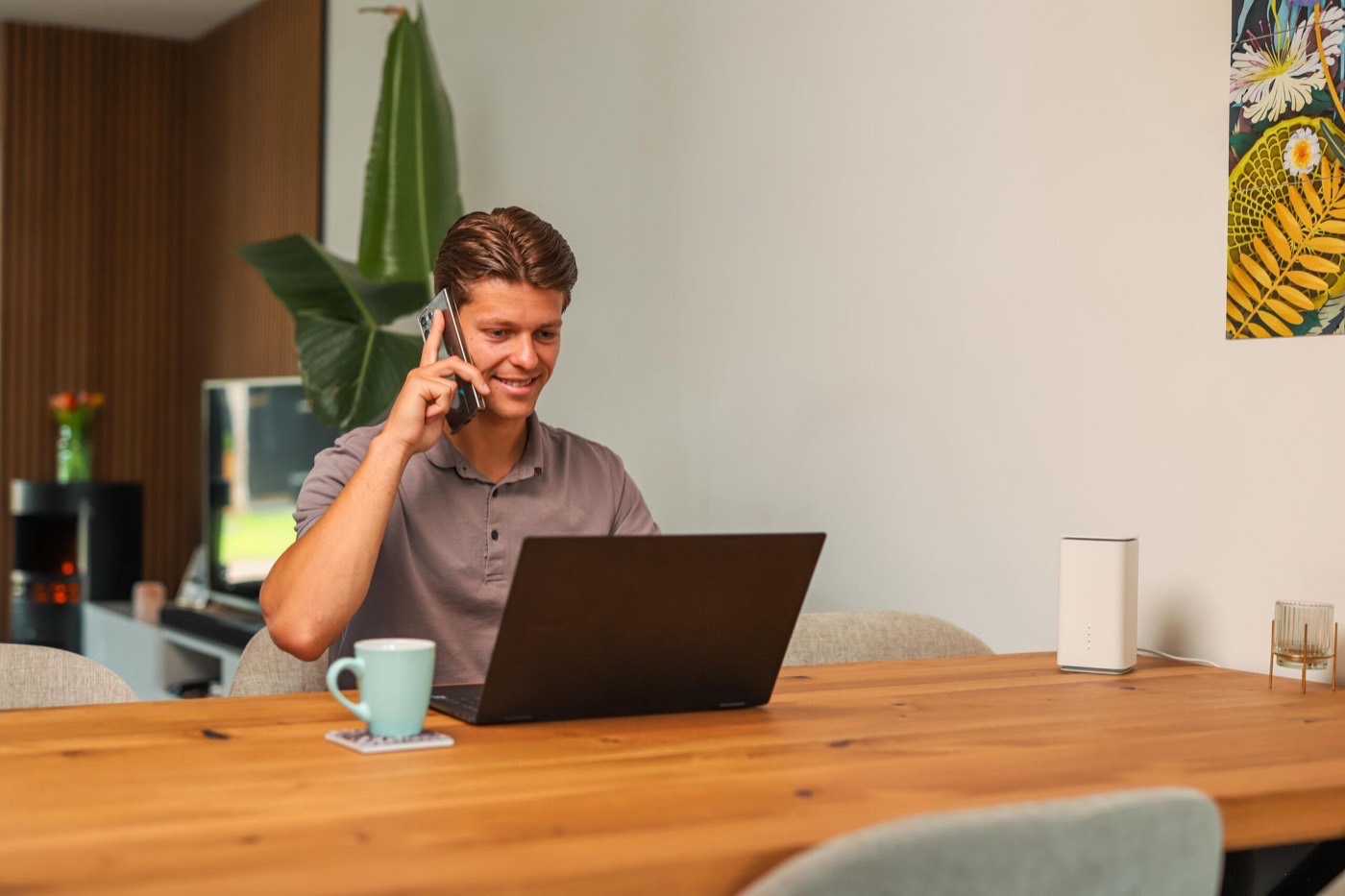 Een persoon zit op een zonnig terras in het buitenland en werkt geconcentreerd op een laptop, met een draagbare router naast zich voor onbeperkt internetten. De omgeving straalt een ontspannen sfeer uit, perfect voor het werken met een mobiel abonnement zonder extra roamingkosten.