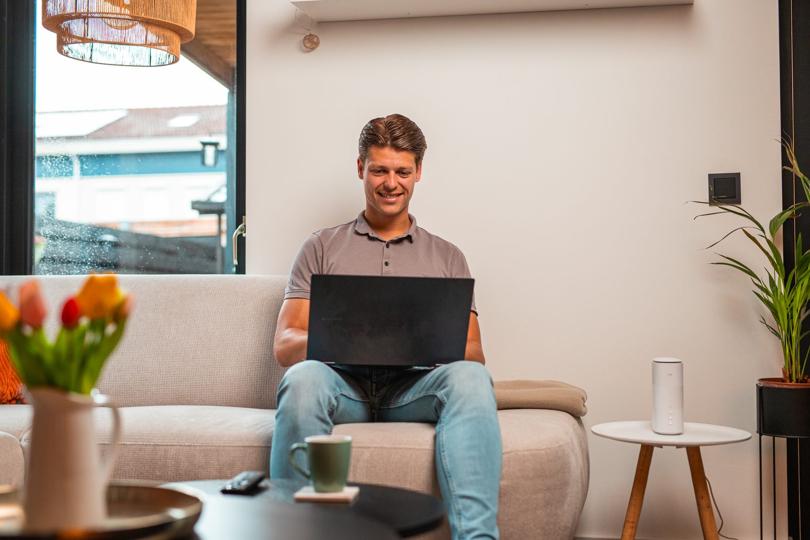 Man zit met een laptop op schoot op de bank, met een modem op de bijzettafel