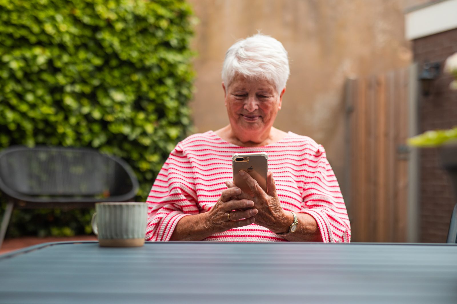 Vrouw kijkt op haar telefoon aan een tuintafel