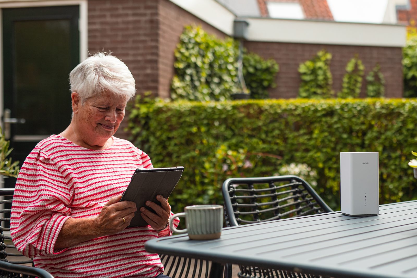 Vrouw met een tablet aan een tuintafel waarop een wit 4G/5G-modem staat
