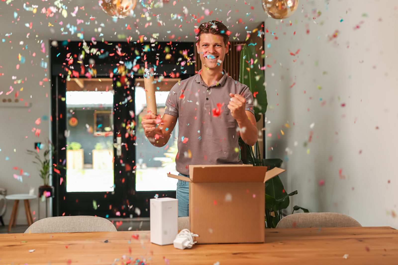 Man viert met confetti het uitpakken van zijn modem uit een verzenddoos