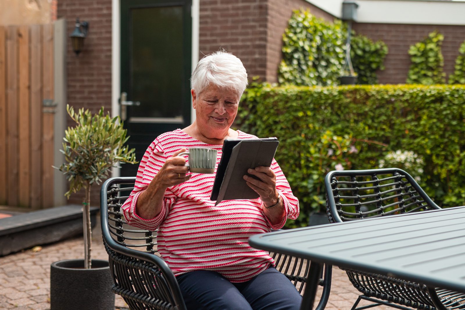 Vrouw zit in de tuin met een kop koffie en een tablet