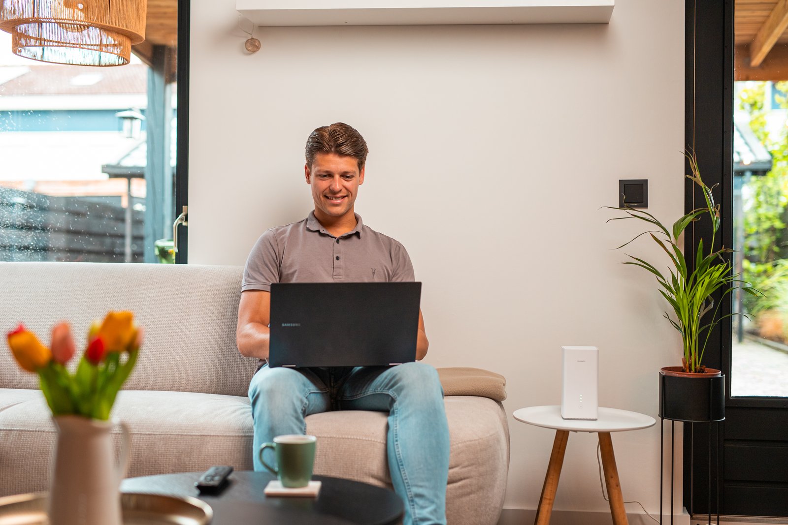 Man werkt op de bank op een laptop, met het 5G-modem op een bijzettafel naast hem