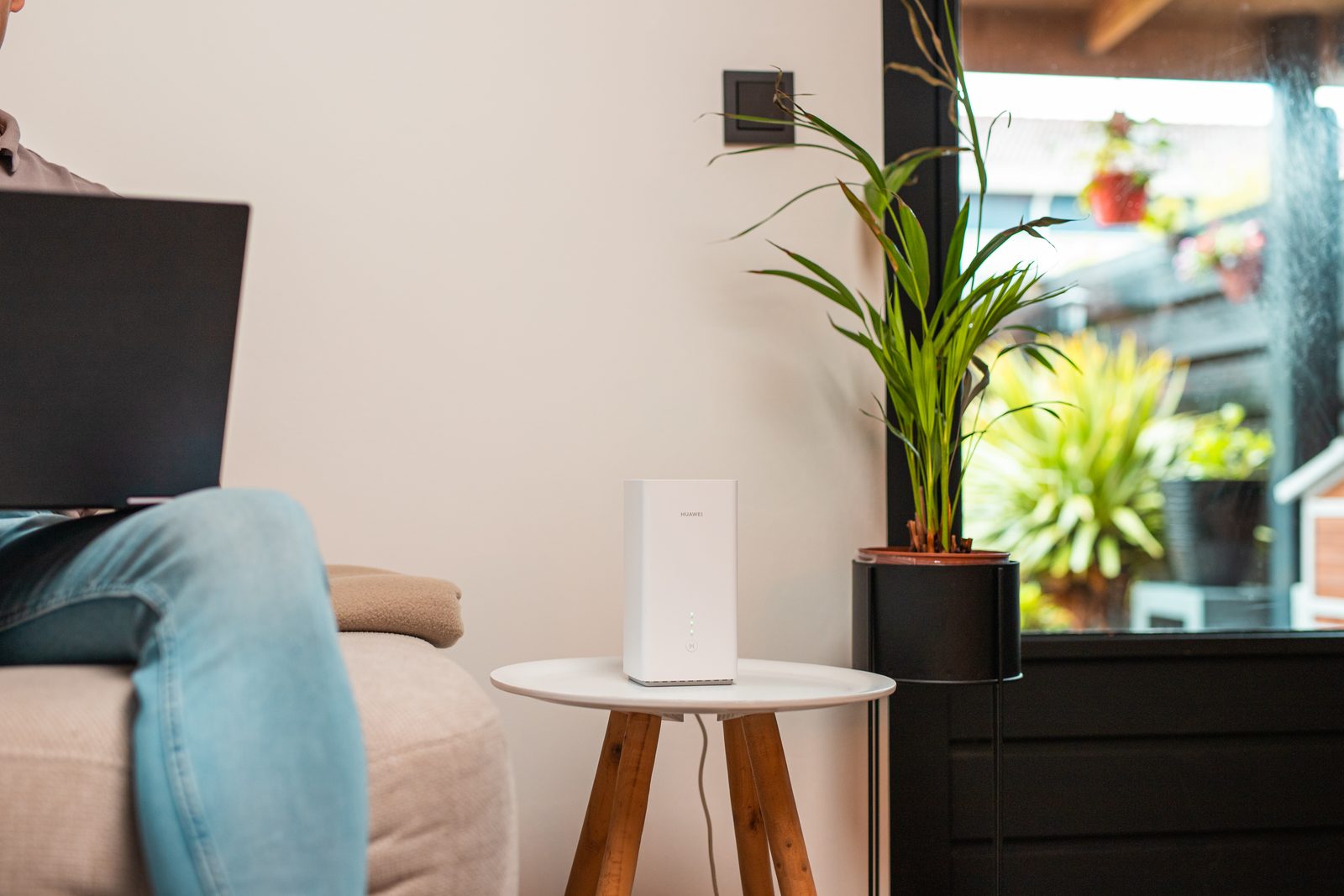 Wit 4G/5G-modem op een bijzettafel naast een plant, met op de voorgrond iemand met een laptop