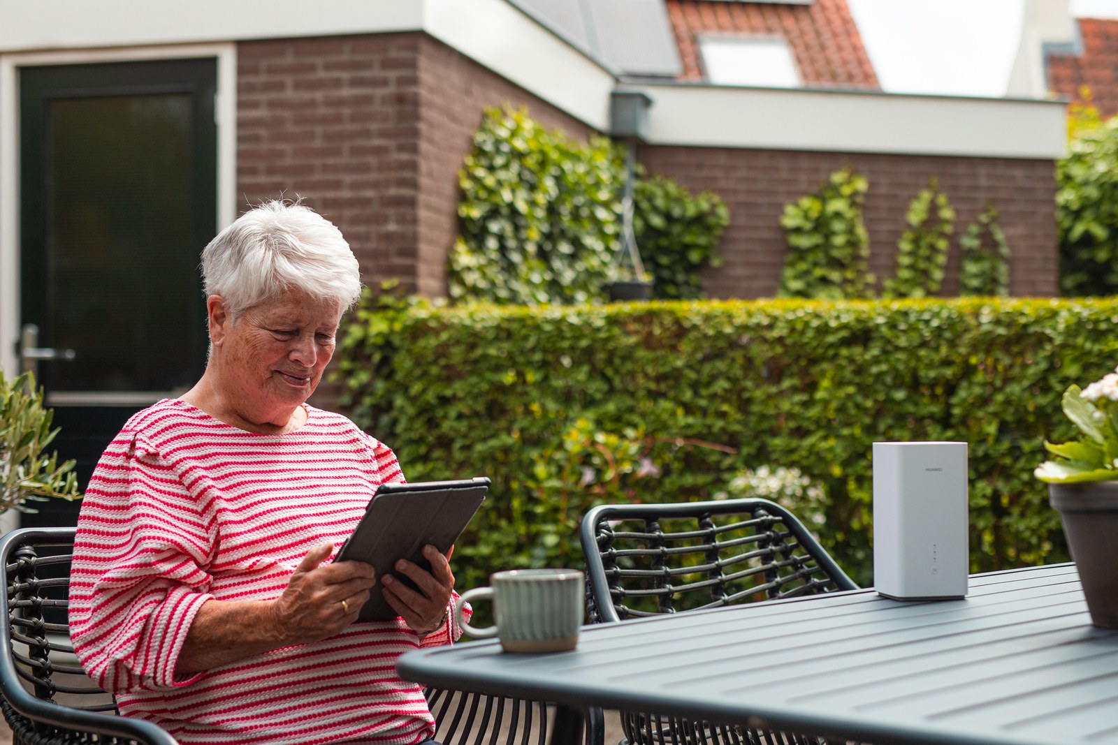Oudere vrouw werkt buiten aan een tafel op een tablet, met het modem naast haar