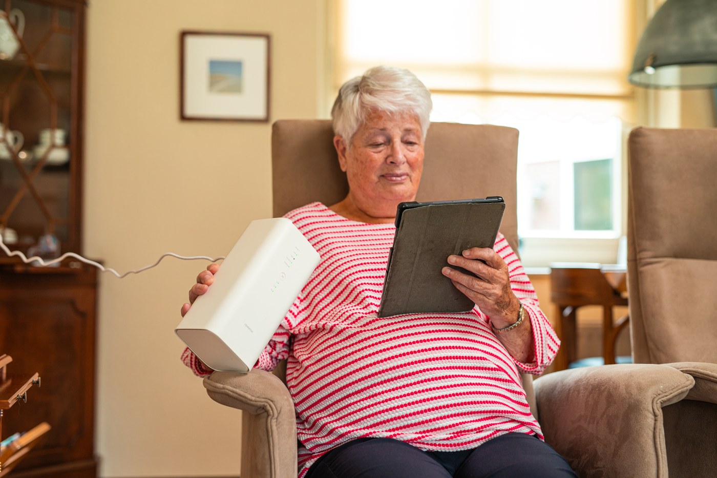 Vrouw in een fauteuil houdt het 5G-modem vast, met een tablet op schoot