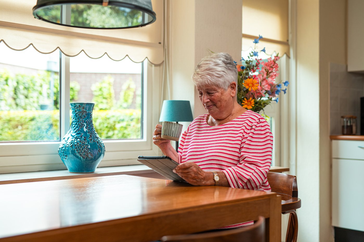Oudere vrouw aan de keukentafel met een tablet, het modem naast haar