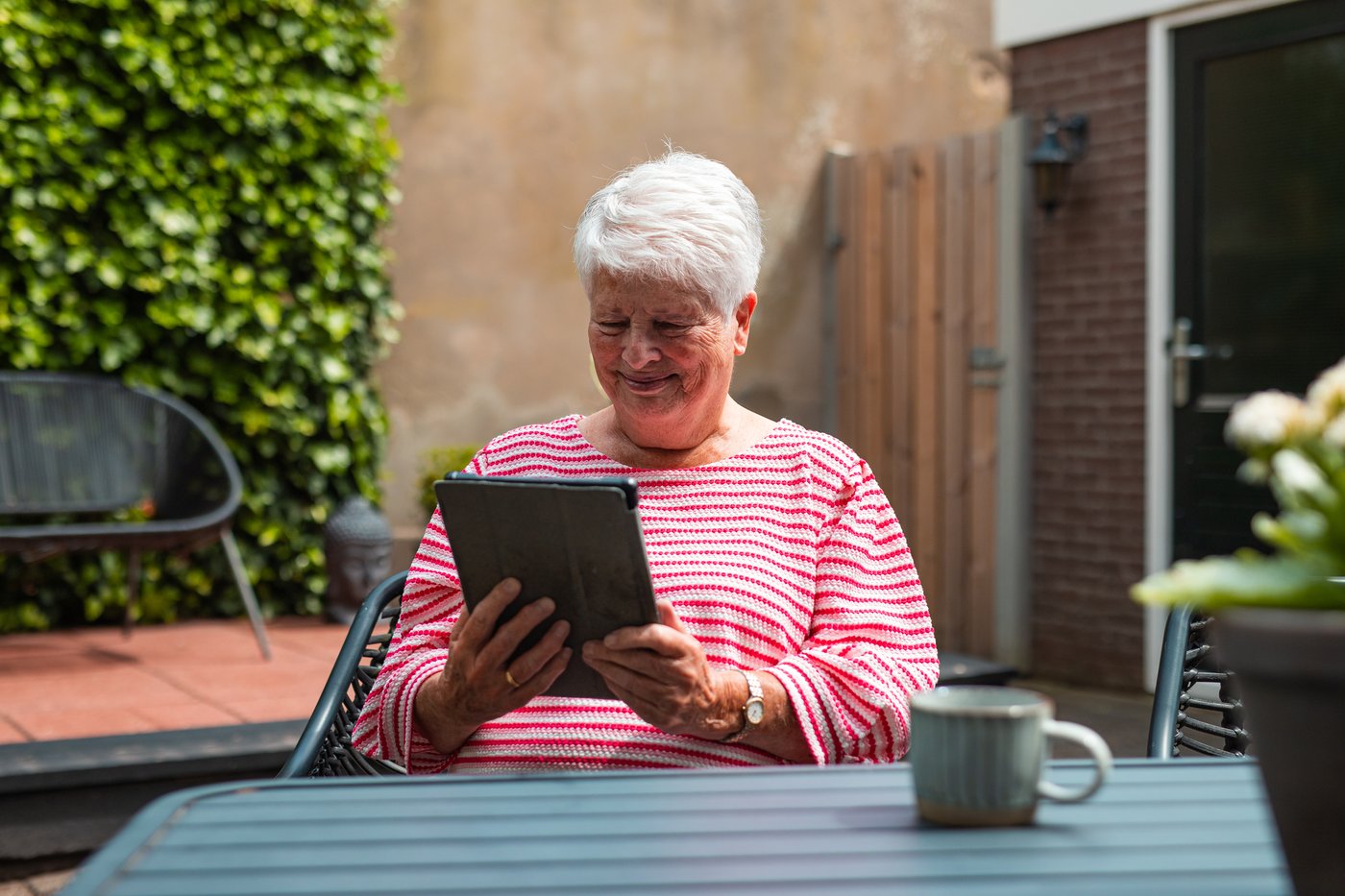 Vrouw zit buiten aan tafel met een tablet en een kop koffie