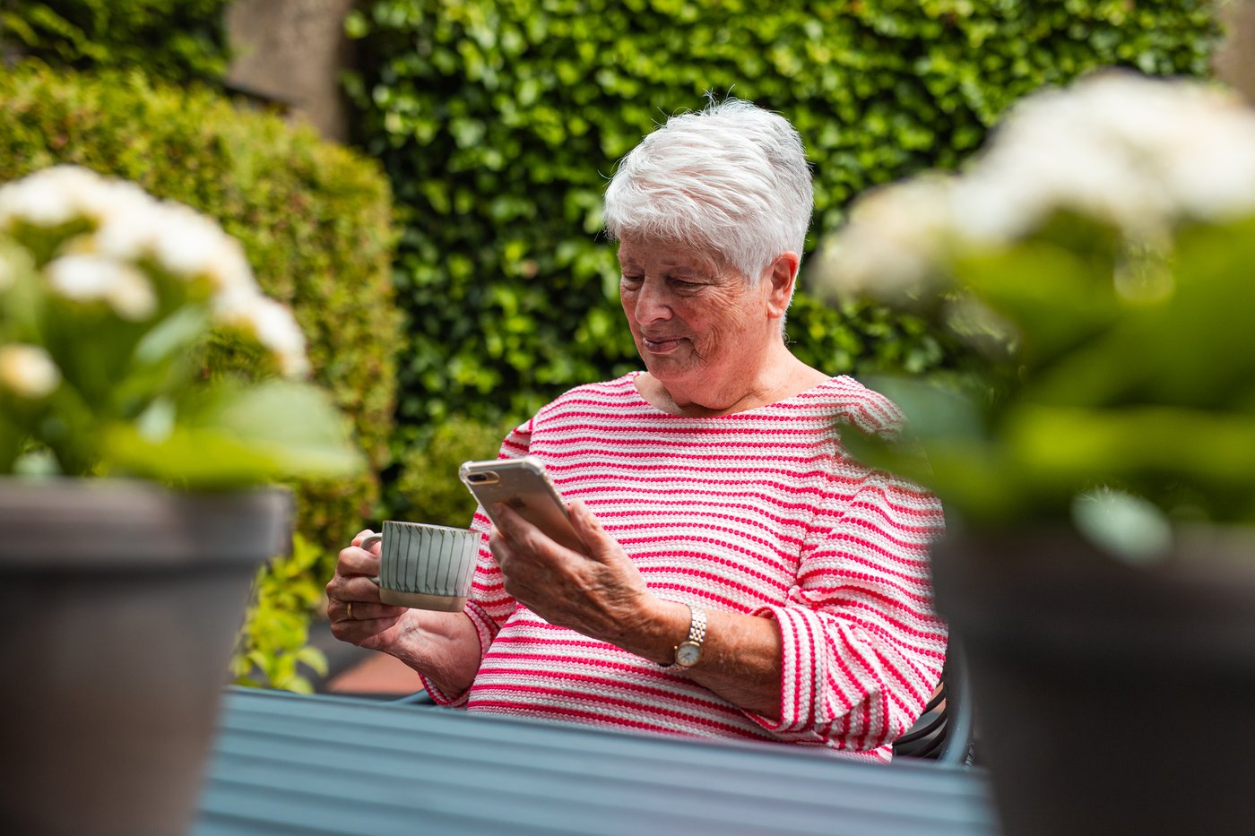Oudere vrouw zit buiten met een telefoon en een kop koffie