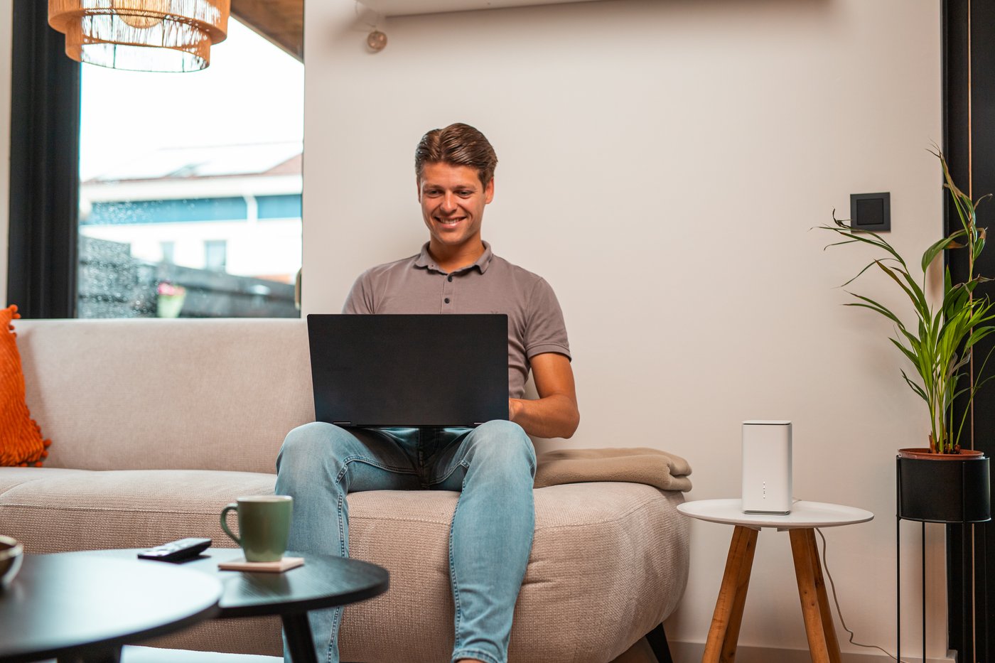 Jonge man met een laptop op de bank, het 5G-modem op het tafeltje naast hem
