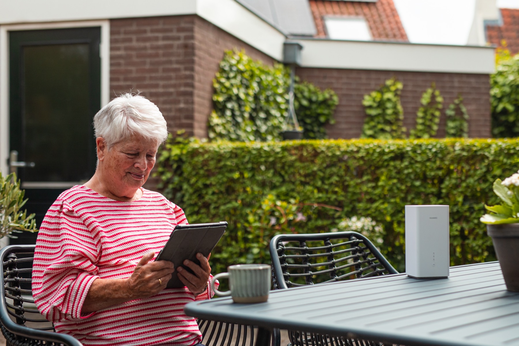 Vrouw met tablet in de tuin, het modem naast haar