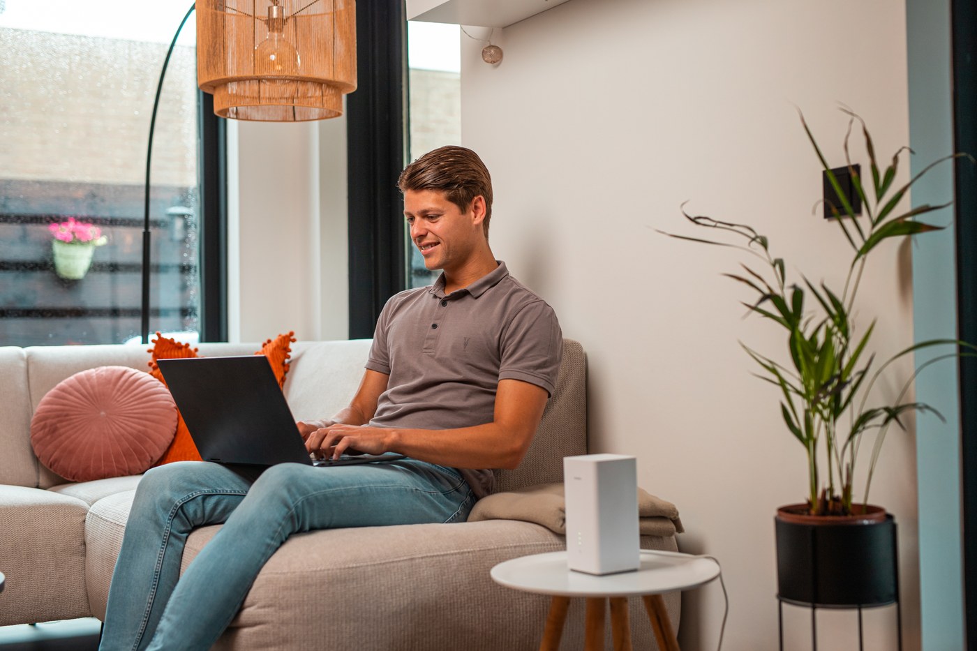 Man op de bank met een laptop, het 5G-modem op het tafeltje naast hem