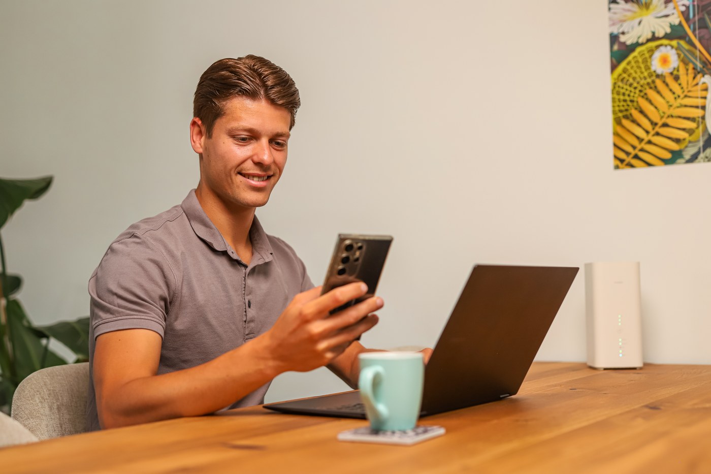 Man aan tafel met telefoon en laptop, het 5G-modem naast hem