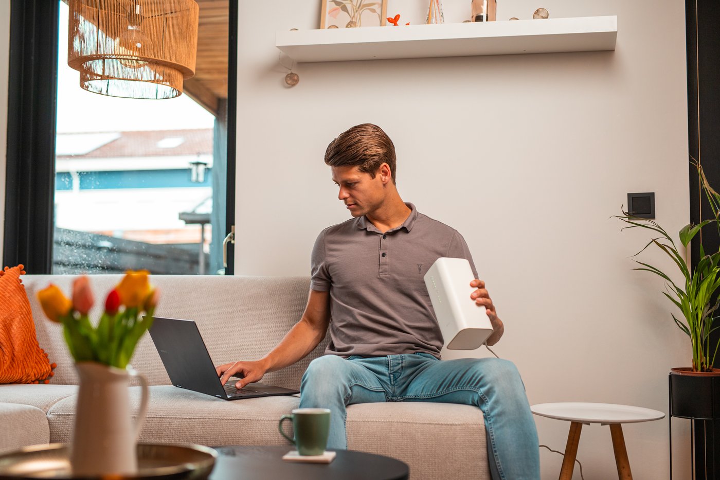 Man op de bank met het 5G-modem in de hand en een laptop op schoot