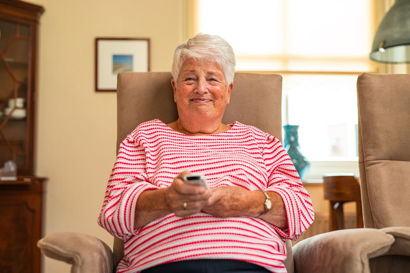 Oudere vrouw in een stoel met de afstandsbediening, het modem op het tafeltje naast haar